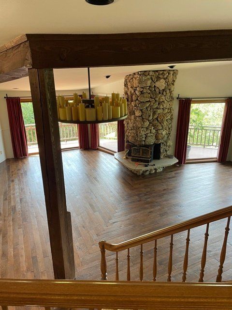 Spacious living room with stone fireplace, wooden floors, and large windows with red curtains.