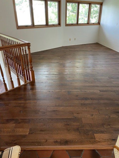Wooden floor with brown planks, a staircase, and windows.