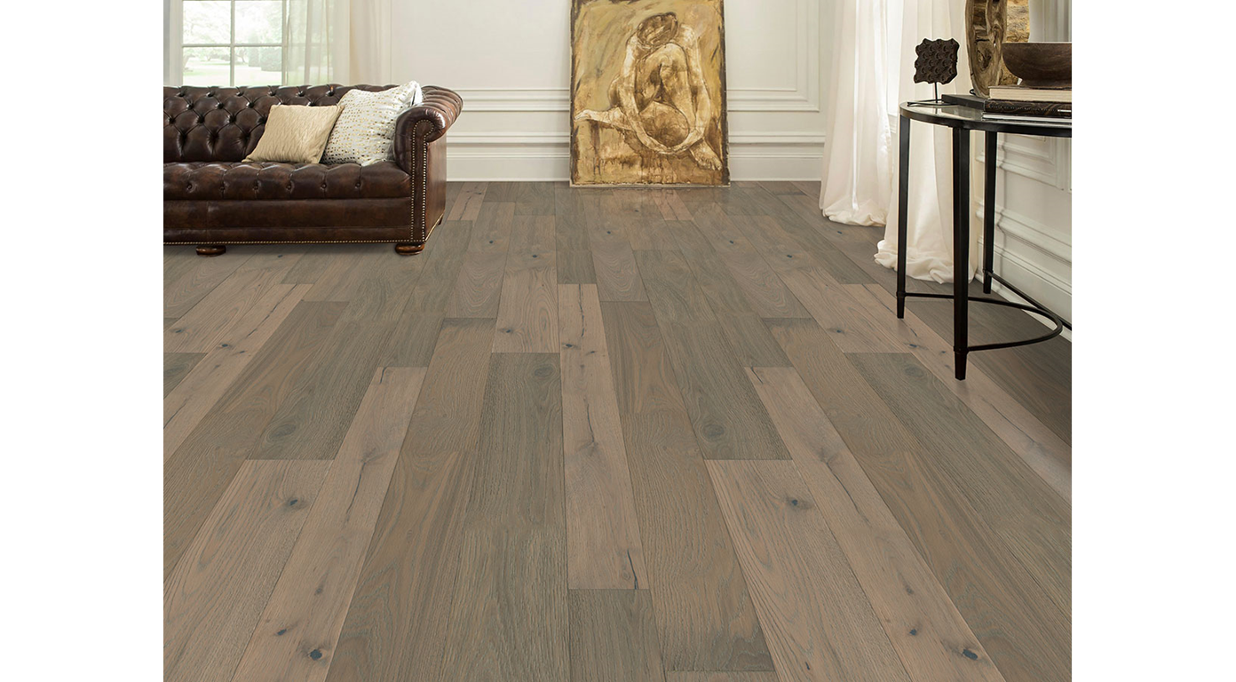 Wooden floor in a living room with leather sofa, antique artwork, and a side table.