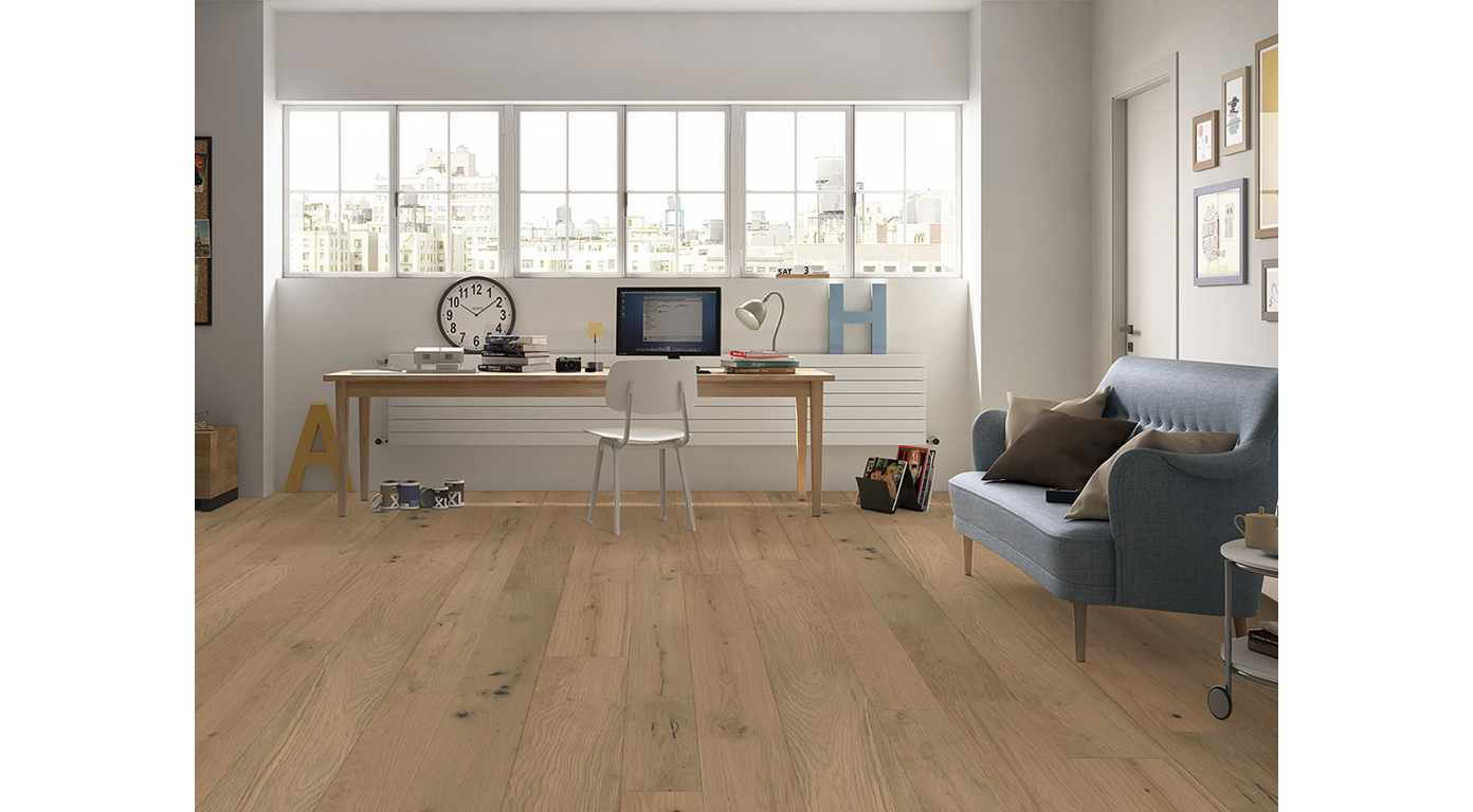 Light wood-floored room with a desk, chair, sofa, and windows. Sunlight streams in.