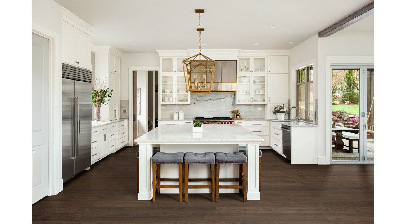 White kitchen with dark wood floor, large island with stools, and gold chandelier.