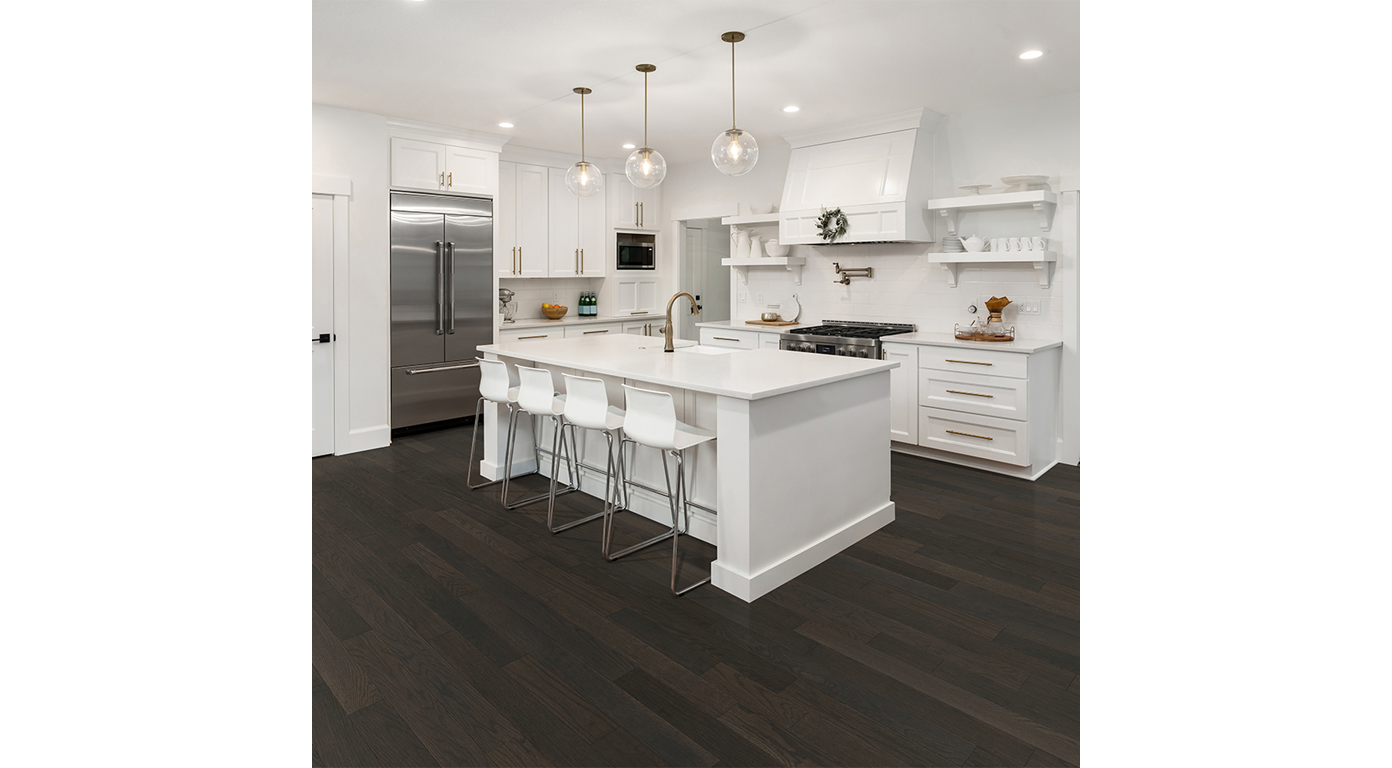 Modern white kitchen with dark wood floors, island with stools, stainless steel appliances.