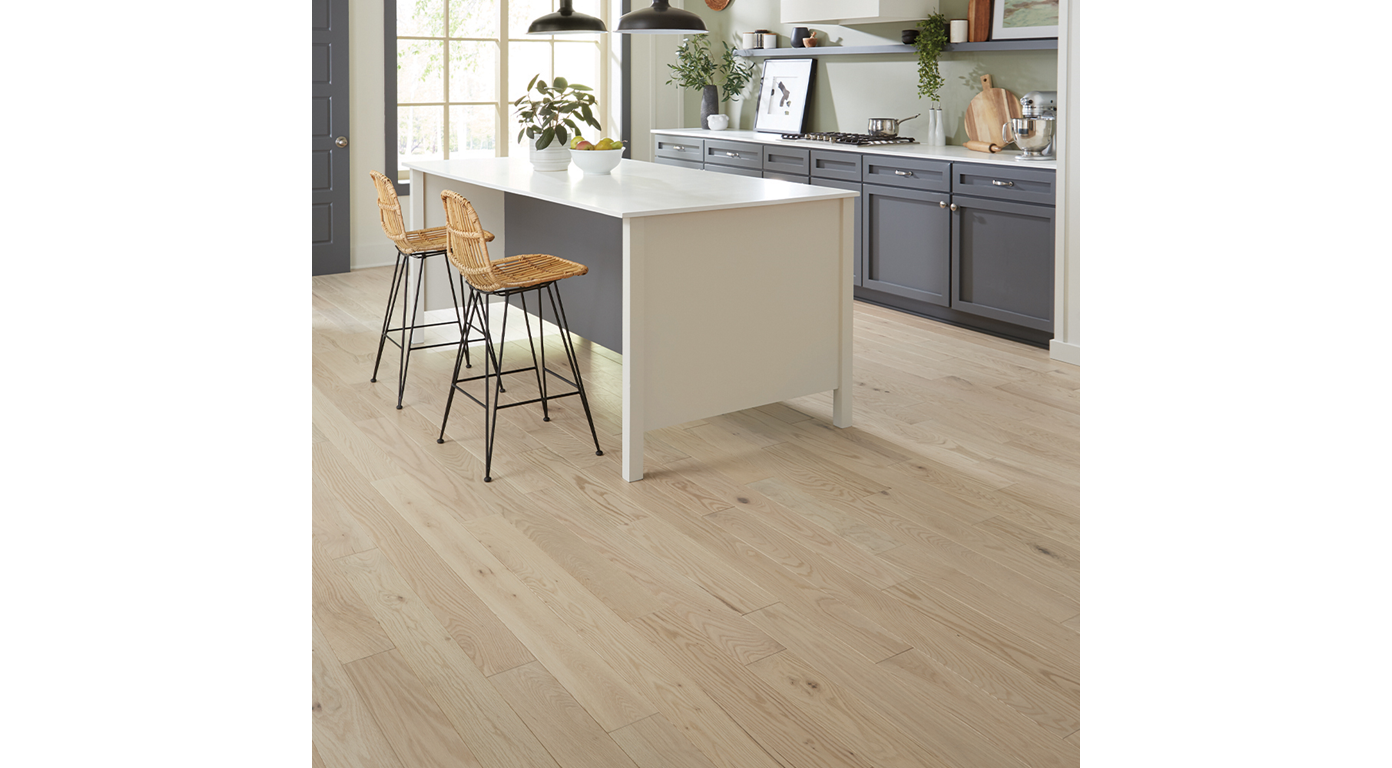 Kitchen with white island, gray cabinets, light wood floor, and bar stools.