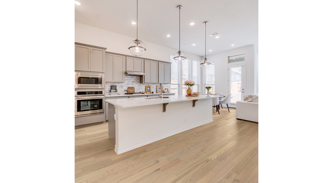 Bright kitchen with white island, light cabinets, and wood flooring. Three pendant lights hang above the island.