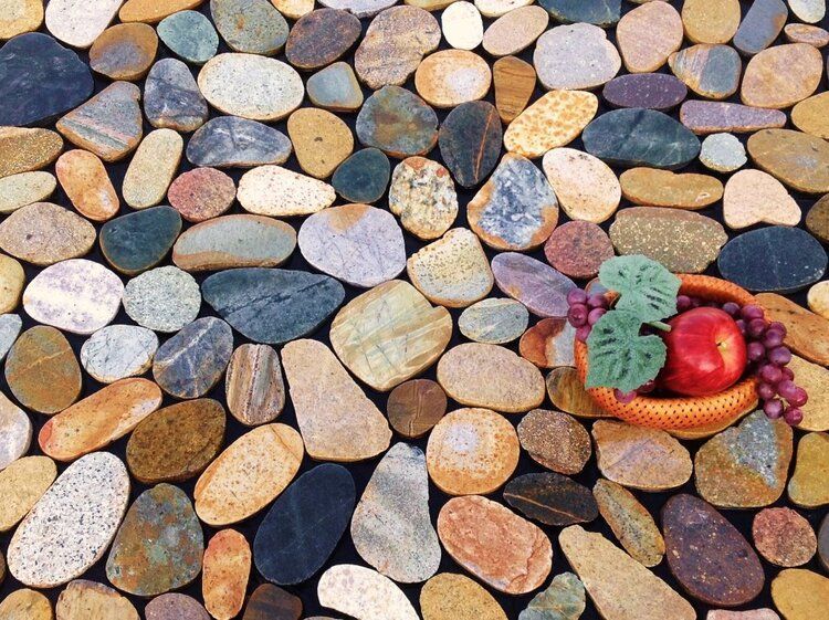 Smooth, colorful river stones with a small basket of fruit.