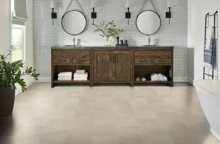 Bathroom with wood vanity, two sinks, round mirrors, and light tile floor.