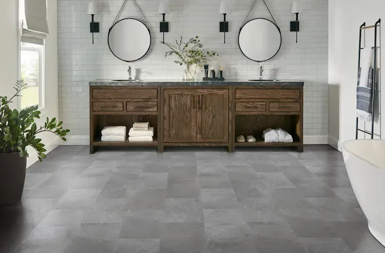 Bathroom with a dark gray tiled floor, a wooden vanity, and two round mirrors.