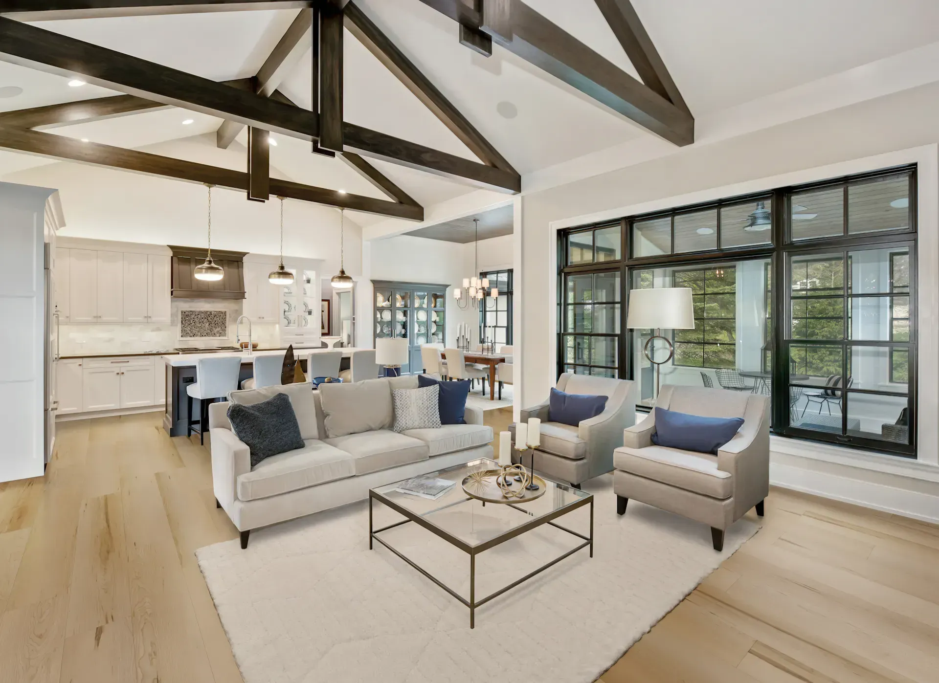 Spacious living room with vaulted ceiling, wood beams, large windows, and open-plan kitchen.