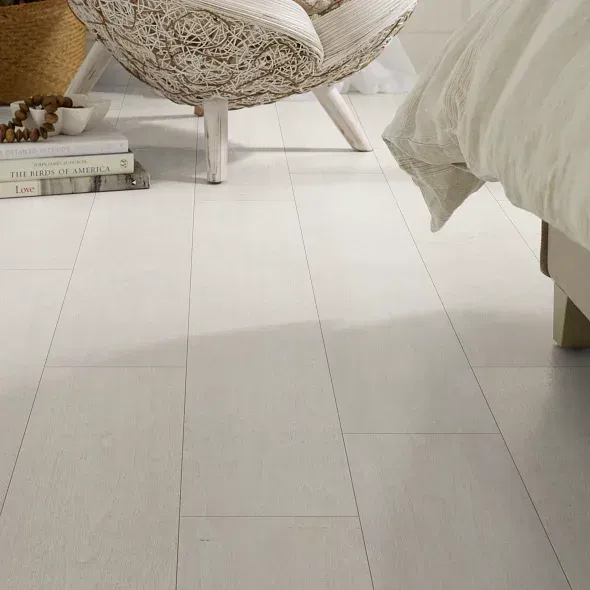 White-washed wood floor. Close-up view. Part of chair and bed in a bright room.