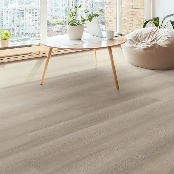 Living room with light wood flooring, round table, laptop, and beanbag chair by a large window.