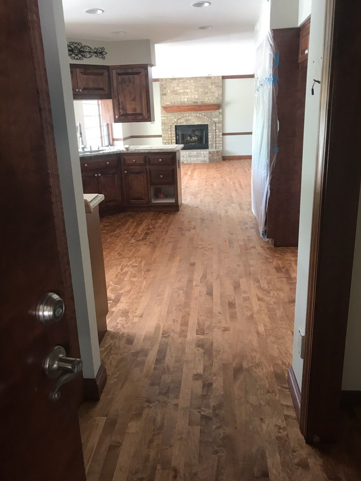 A view from a doorway into a kitchen and living room with hardwood floors and a stone fireplace.