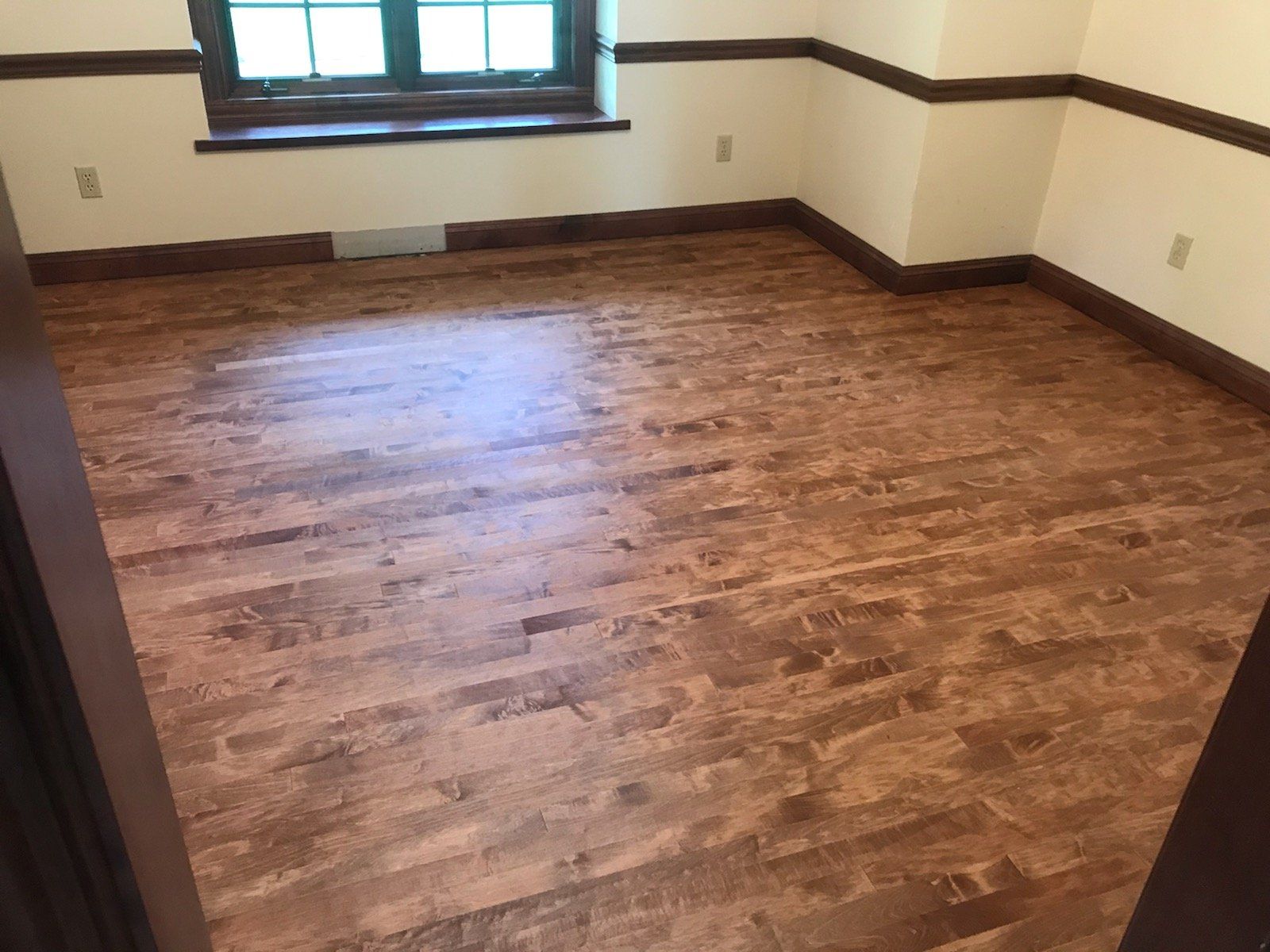 Room with stained wood floors, window, and light beige walls with dark wood trim.