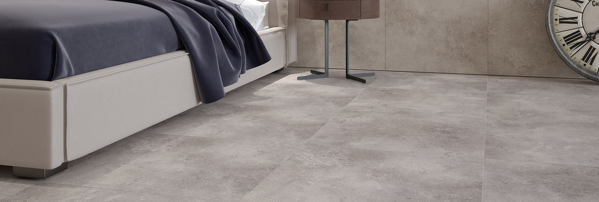 A bedroom with a bed, lamp, and wall clock. The floor is made of light-colored tiles.