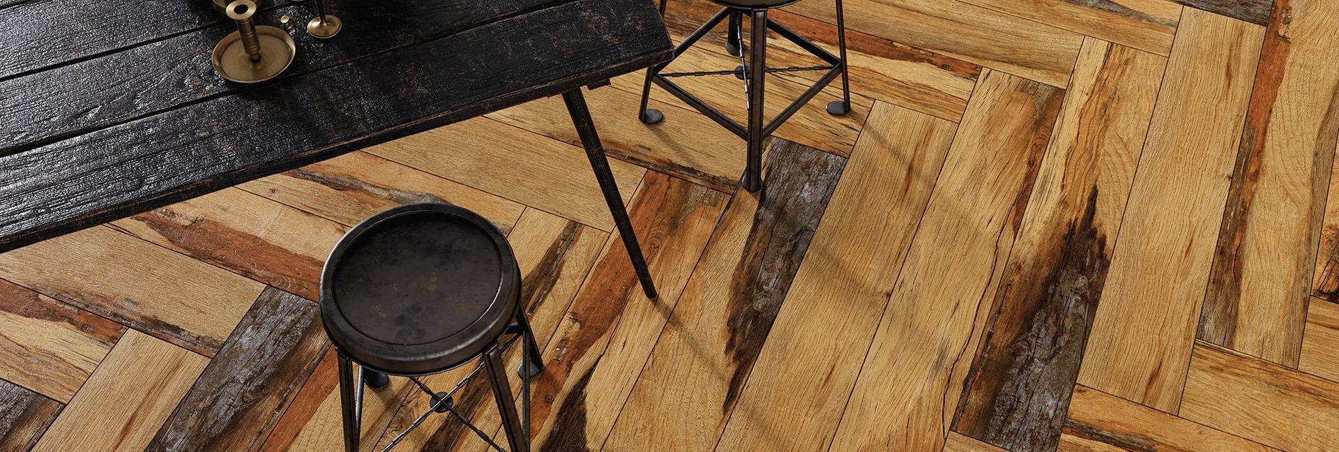 Overhead shot of a room with a black table, metal stool, and wooden herringbone floor.