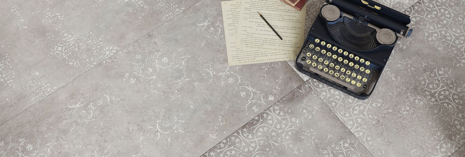 An old typewriter next to a notepad and pen on a textured, gray surface.