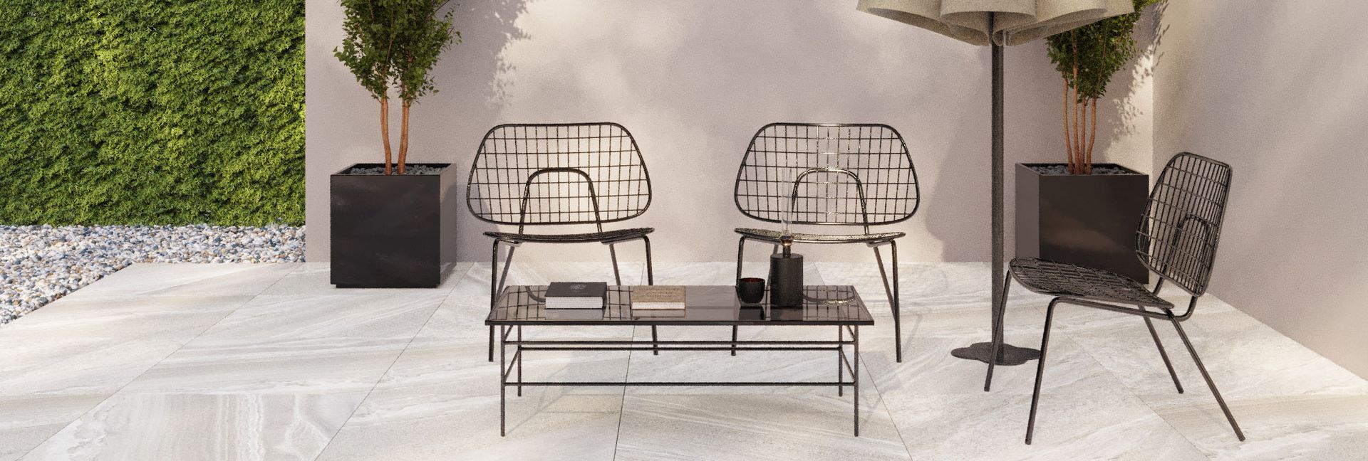 Outdoor seating area with wire-framed chairs, coffee table, and umbrella on a stone patio with a green hedge background.