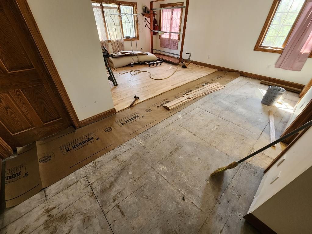 Interior view of a room undergoing floor renovation, with exposed subfloor and partially installed planks.