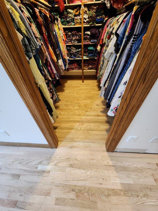 Walk-in closet filled with clothes. Oak wood floor and door frames, colorful array of clothing.
