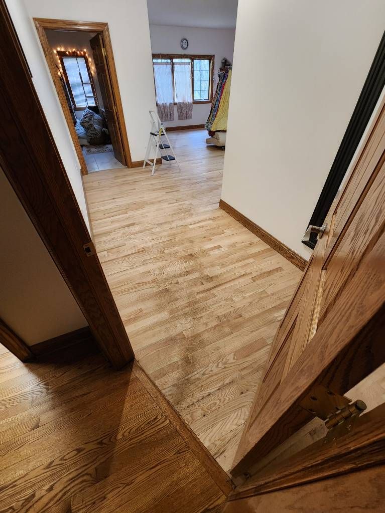 Wooden hallway with light brown floors, leading to another room, doorway on either side.