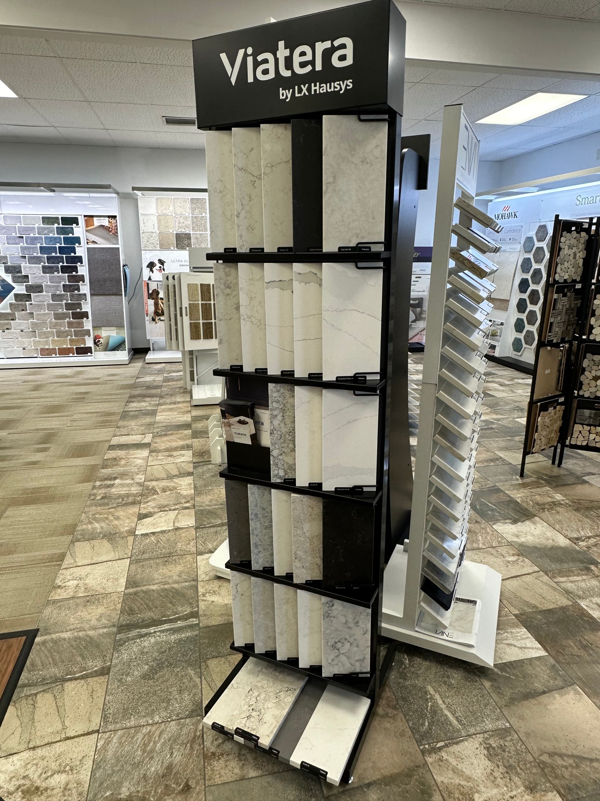 A display stand showcasing various Viatera tile samples in a showroom setting.