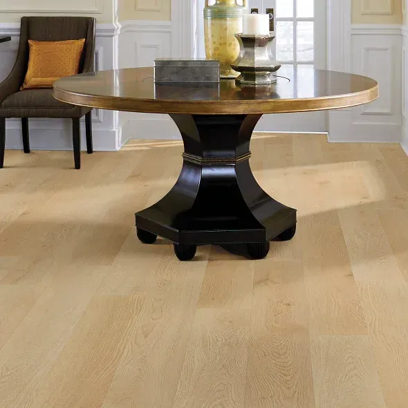 Round wooden table with dark pedestal base on light hardwood floor, chair in background.