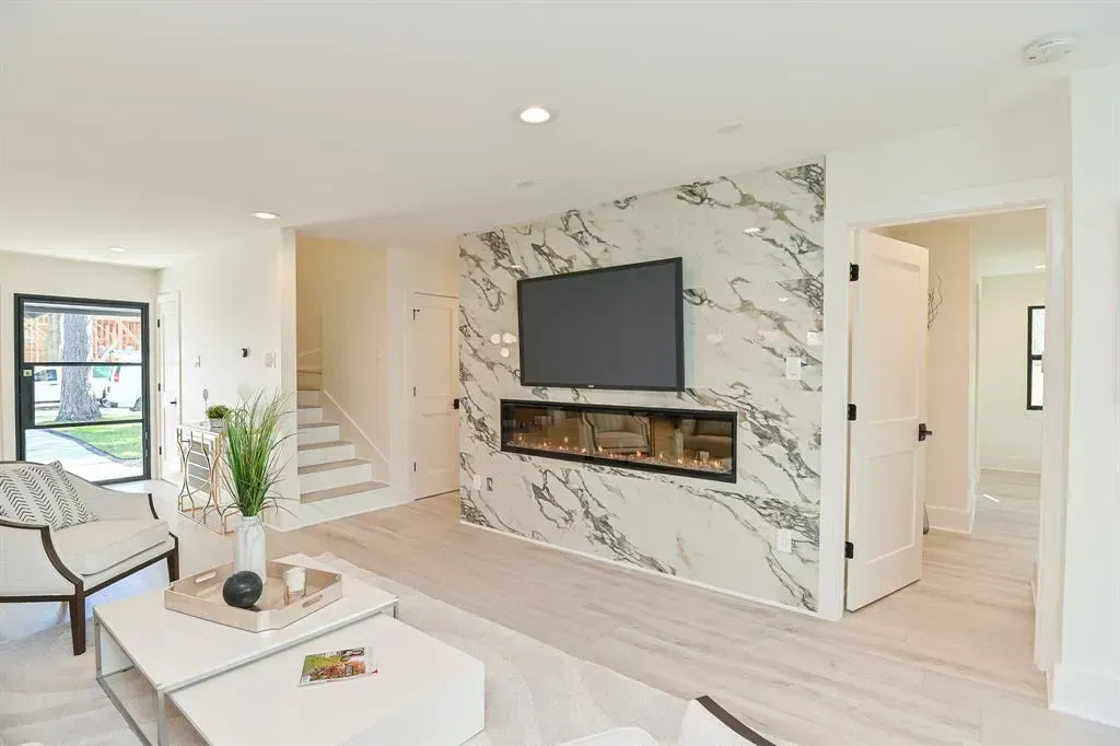 Living room with marble accent wall, fireplace, and mounted TV. Modern design with white and gray tones.