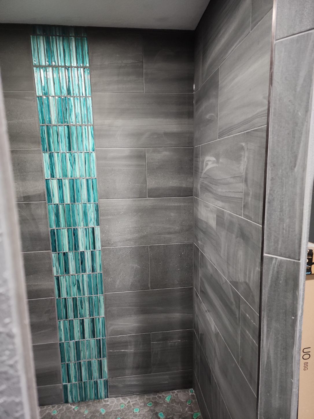 Gray tiled shower with vertical turquoise accent strip.