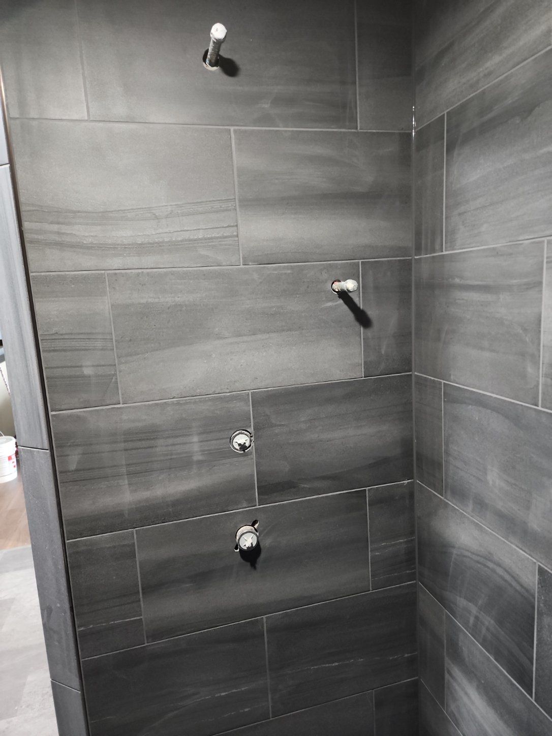 Dark gray tiled shower with multiple pipe stubs protruding from the wall.