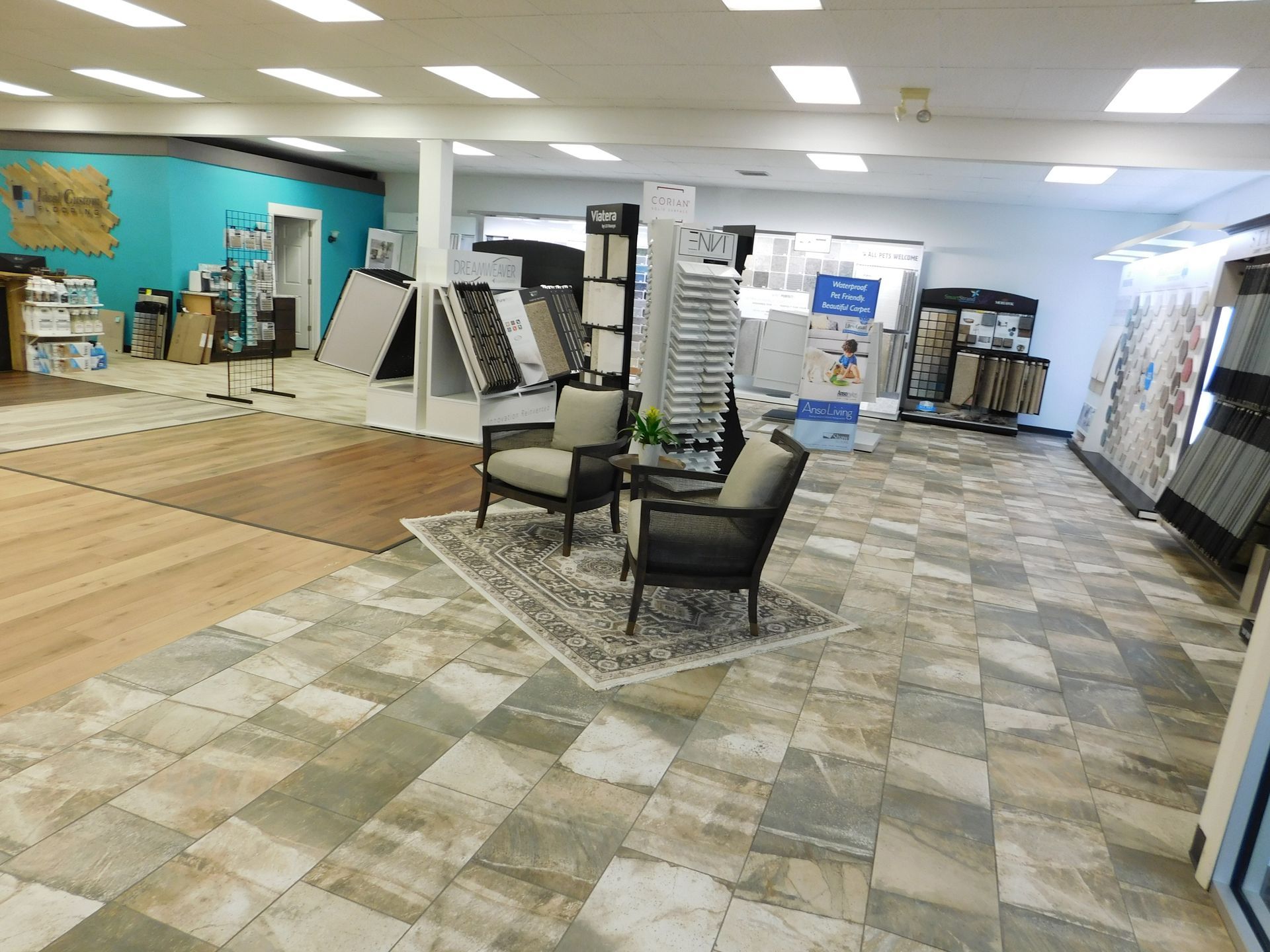 Interior of a flooring store. Displayed samples, two chairs on a rug, and a wood and tile floor.