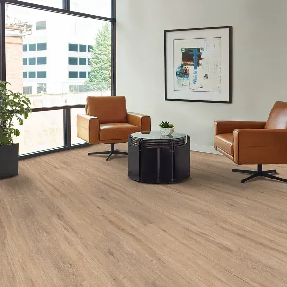 Cozy living room with light wood-look flooring, two brown leather chairs, a dark round table, and a window.