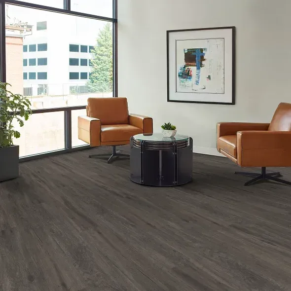 Two leather armchairs and a small table on dark wood flooring in a room with a large window.