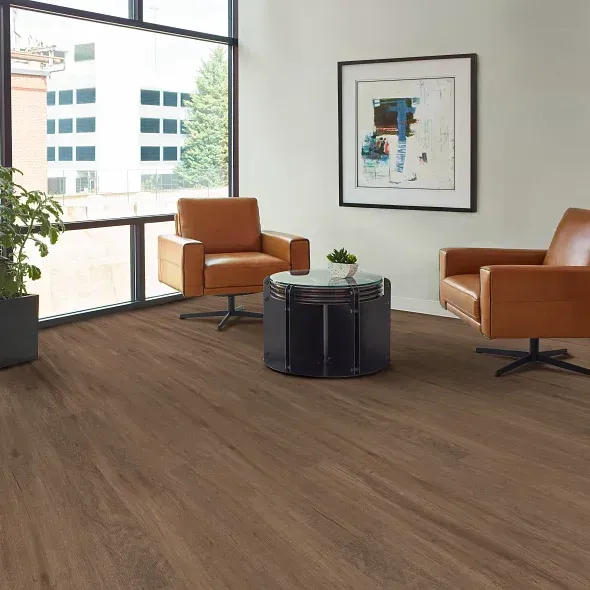 Room with brown flooring, two leather chairs, and a small table, near a large window.
