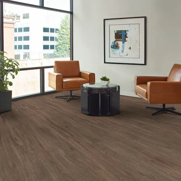 Two leather chairs face a dark wood-look floor, with a small table between them. Large window and art present.