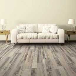 Cream sofa with pillows, flanked by lamps on wooden tables, on wood-look flooring against a cream wall.