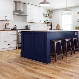Kitchen with wood floors, white cabinets, blue island, and bar stools.