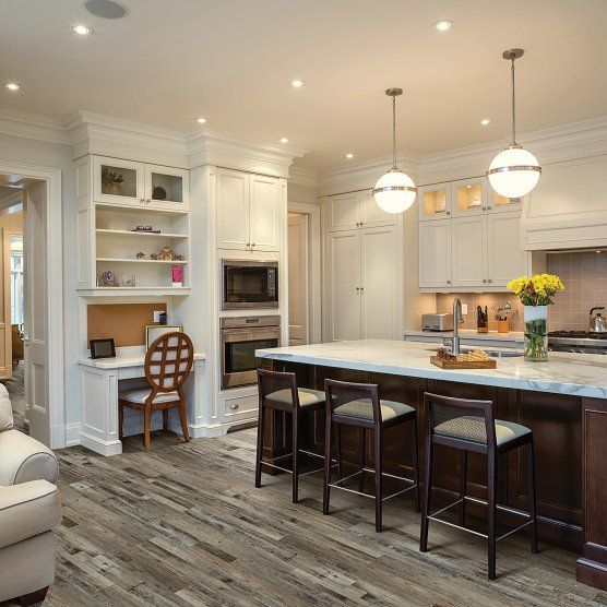 Elegant kitchen with a dark-wood island, white cabinets, built-in desk, hardwood floor, and pendant lights.
