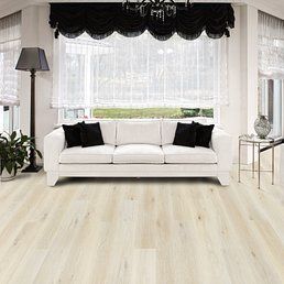 Light wood floor in a modern living room with white couch, black pillows, and sheer window curtains.
