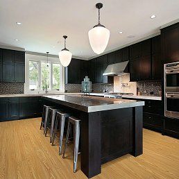 Kitchen with dark cabinets, light island, and pendant lights; wood floors and stainless steel stools.