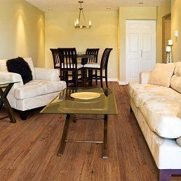 Living room with wooden floor, two cream sofas, glass coffee table, dining table, and a chandelier.
