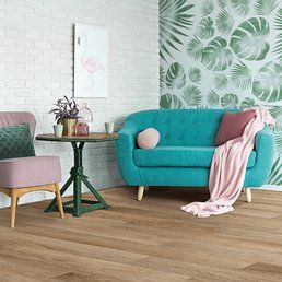 Living room with a turquoise sofa, pink chair, green table, and wooden floor. Palm leaf wallpaper.