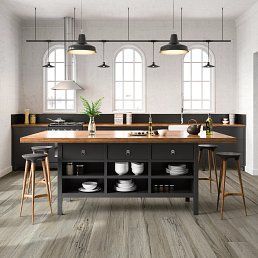 Kitchen with island, dark cabinets, wooden countertop, gray flooring, and arched windows.