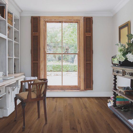 Room with hardwood floors, a window with shutters, a desk with chair, and a decorative table.