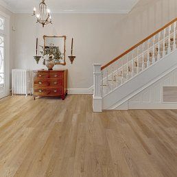 Hallway with wood floor, staircase, chest, mirror, candles. Beige walls, light wood floor.