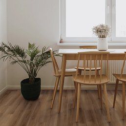 Dining room with wooden table and chairs, window, plant, and vase of flowers.