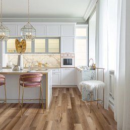 White kitchen with marble backsplash, golden accents, pink velvet stools, and wooden floor.
