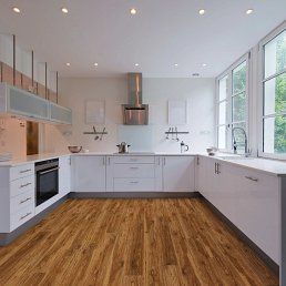 White modern kitchen with wood-look flooring, white cabinets, oven, and large windows.