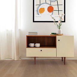Mid-century modern cabinet with cream-colored drawer and door, wooden top. Flowers, cups, and artwork on display.