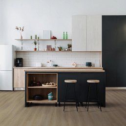 Modern kitchen with black island, light wood cabinets, and white walls. Two stools sit at the island.