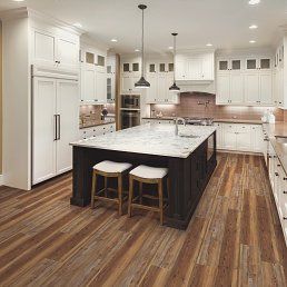 A spacious kitchen with white cabinets, a dark island with stools, and wood-look flooring.
