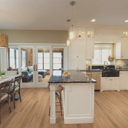 Bright kitchen with an island, white cabinets, and wooden floor, with a view to a living room.